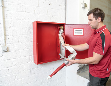 Das Bild zeigt einen Brandschutztechniker bei der Überprüfung eines Wandhydranten in einem Treppenhaus